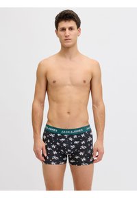 Νεαρός άνδρας που στέκεται στραμμένος προς τα εμπρός, φοράει μαύρα boxers με λουλουδάτο μοτίβο και πράσινη μέση με την επιγραφή Jack & Jones.