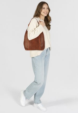 Sac à épaule en cuir tressé marron avec une texture en maille, forme arrondie et une seule bandoulière. Associé à un pull crème et un jean bleu clair.
