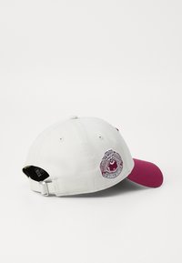Fehér szövetből készült baseballsapka bordó napellenzővel. Bordó és ezüst hímzett logóval ellátott folt található a hátán.