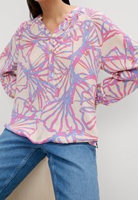 Blouse légère rose pâle avec un motif floral abstrait coloré en bleu et fuchsia. Comprend un col en V, une patte de boutonnage et des manches amples.
