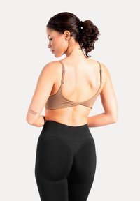 Brązowy, miękki biustonosz z regulowanymi ramiączkami i misternym wzorem na plecach, zestawiony z czarnymi legginsami o wysokim stanie.