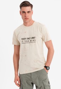 Camiseta de un beige claro con un patrón texturizado, con texto en negro: "TU ÚNICO LÍMITE ERES TÚ MISMO." Diseño de manga corta y cuello redondo.