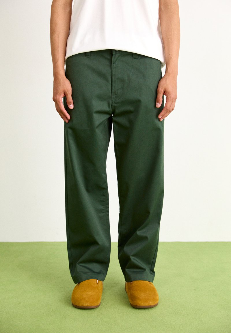 Pantaloni verzi, lejere, dintr-un material neted, cu fața plată și buzunare laterale, asortați cu pantofi slip-on din piele ante bej.