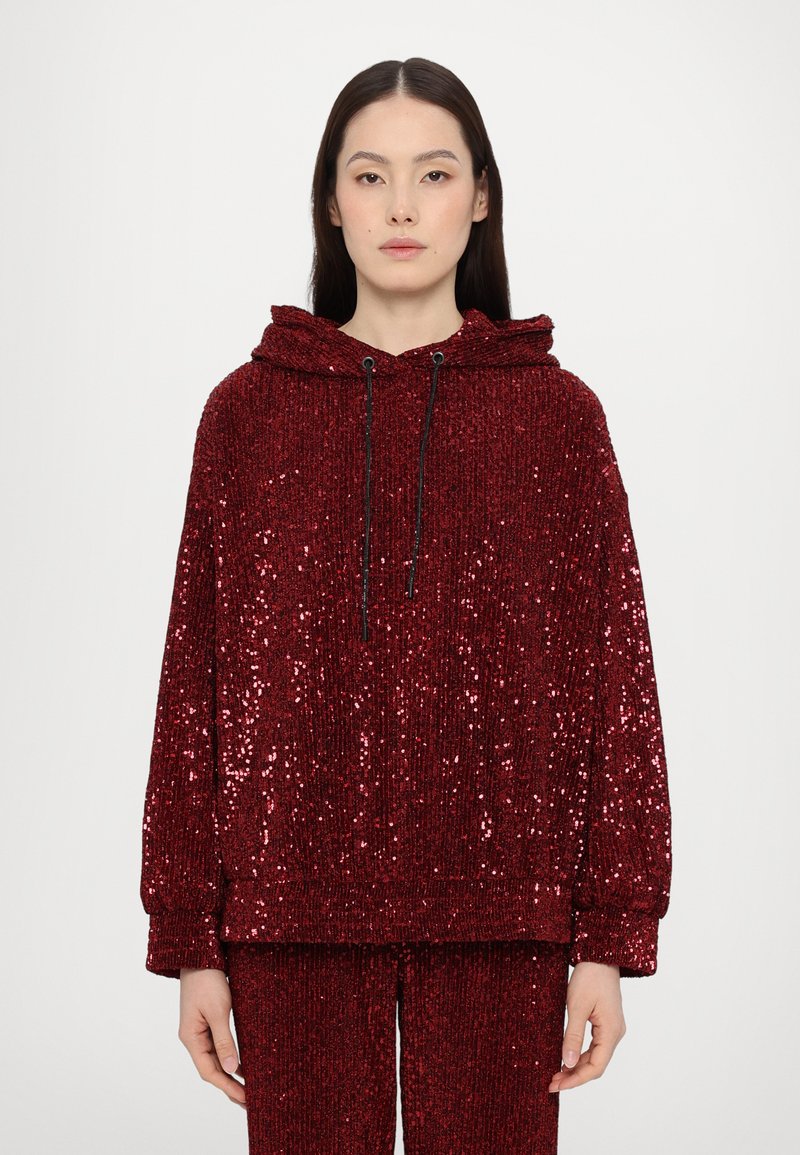 Red sequined hoodie with a textured surface, adjustable drawstring, and loose fit. Features long sleeves and ribbed cuffs at the hem.