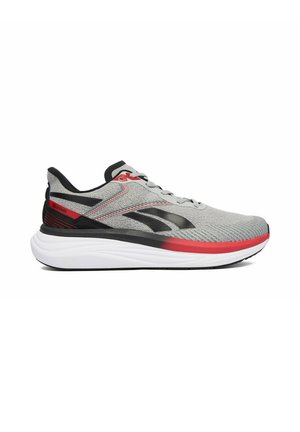 Zapatilla de correr Reebok en gris y negro con detalles en rojo y suela blanca, vista de lado sobre un fondo blanco.