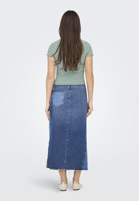 T-shirt rayé vert associé à une jupe maxi en denim bleu, dotée d'une poche arrière et d'un ourlet effiloché, portée avec des chaussures de couleur claire.