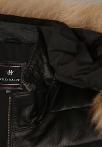 Veste en cuir noir avec fermeture éclair et capuche en tissu noir attachée, ornée d'un bord en fourrure brune, affichant l'étiquette de la marque Felix Hardy et le tag taille moyenne.