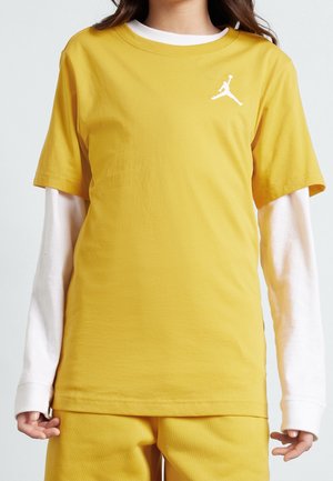 Child wearing layered white long-sleeve top under yellow short-sleeve shirt and yellow pants with white basketball logo on chest.