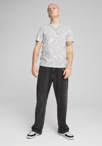 Grå camouflage-mønstret t-shirt med korte ærmer, parret med mørkeblå, løstsittende jeans og sort-hvide sneakers. Tyk sølvkæde om halsen.