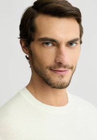 Világos színű, kötött kerek nyakú pulóver, puha anyagból készült, laza szabással és bordázott textúrával a nyakrészen.
