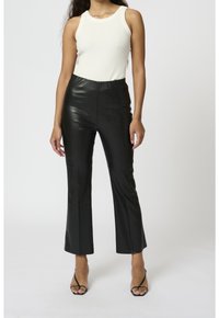 Mustat keinonahkaiset leveälahkeiset housut, joissa on korkea vyötärö, sileä pinta ja ommeltu yksityiskohta, yhdistetty valkoiseen ribbipaitaan.