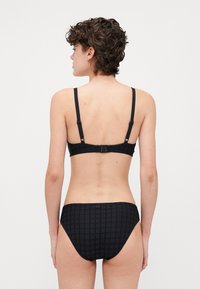 Svart bikini-set med en strukturerad mönster. Toppen har justerbara remmar och en hake-stängning, medan botten har en medelhög skärning.
