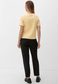 Żółta koszulka z krótkim rękawem o prostym kroju, z małym, wytłoczonym wzorem na plecach. Połączona z czarnymi spodniami slim fit.