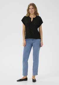 Black short-sleeve top with diamond pattern and a keyhole neckline, paired with light blue straight-leg jeans and black flats.
