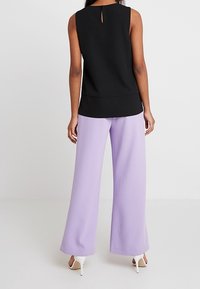 Czarna bezrękawnikowa bluzka z wycięciem na plecach, w parze z jasnopurpurowymi szerokimi spodniami i białymi szpilkami. Gładka faktura tkaniny.