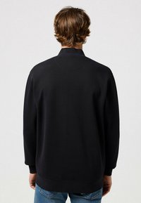 Sudadera negra de cuello alto, de manga larga y puños de canalé, hecha de una tela suave y texturizada.