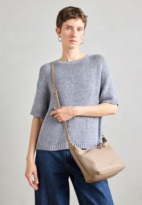 Suéter de punto gris claro con mangas cortas, combinado con denim azul suelto y un bolso de hombro de cuero beige con cierre de cremallera.