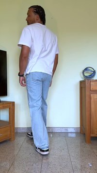 T-shirt blanc, jeans bleu clair, et baskets noires. Motif à pois sur les jeans, coupe décontractée, et longueur moyenne. Debout à l'intérieur avec des meubles à proximité.