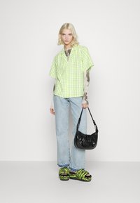 Camisa de manguitas curtas em xadrez verde e branco, jeans azul claro, mala de patente preta e sandálias de plataforma com padrão de zebra preto e verde.