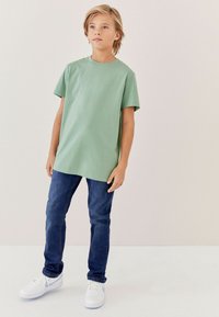 Kortärmad mintgrön t-shirt, avslappnad passform, ihopparad med mörkblå jeans och vita sneakers. Enkelt design utan mönster eller detaljer.