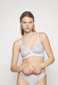 Soutien-gorge sans fil violet clair de forme triangulaire, en tissu lisse, avec des bretelles ajustables et une bande ornée d'un logo en bas.