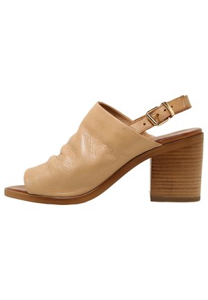 Sandale à talon ouverte en cuir beige avec un talon bloc et une sangle de cheville ajustable avec boucle dorée.