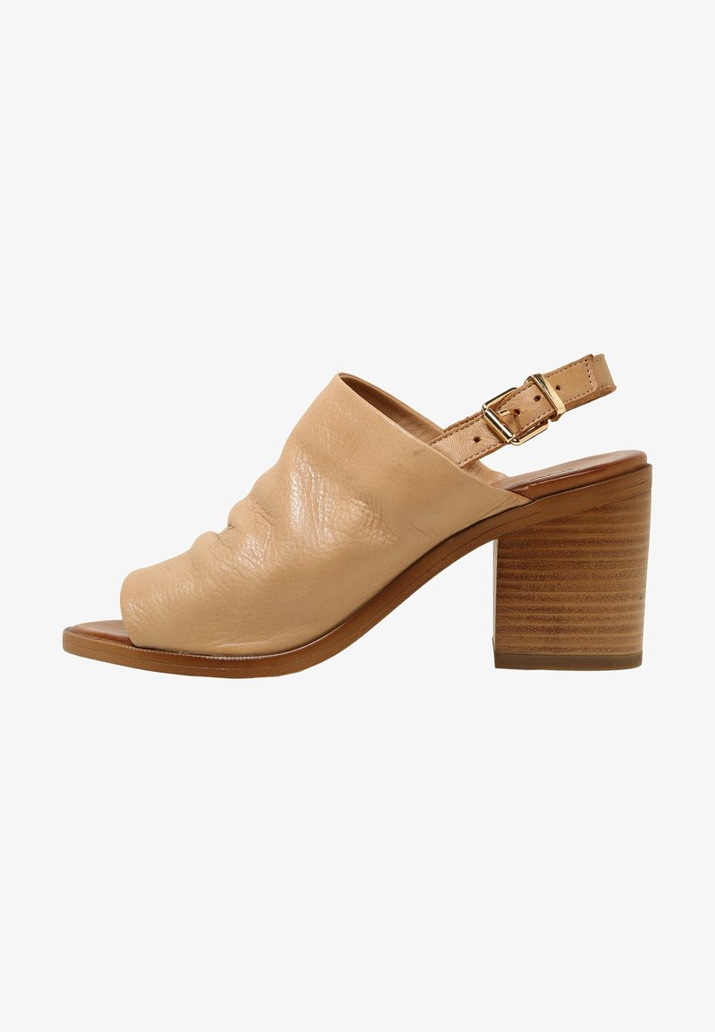 Sandale à talon ouverte en cuir beige avec un talon bloc et une sangle de cheville ajustable avec boucle dorée.