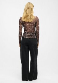 Haut à manches longues, transparent, de couleur marron avec un motif texturé ; associé à un pantalon noir taille haute, large et en denim.