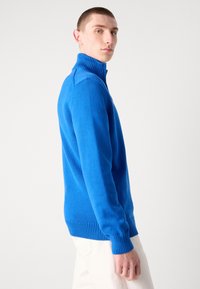 Blauer Strickpullover mit hochliegendem Rippkragen, langen Ärmeln sowie Rippbündchen und -saum. Glatte Textur, taillierte Passform. Unifarben ohne Muster.