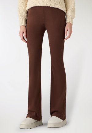 Pantaloni marroni a zampa d'elefante realizzati in tessuto morbido, caratterizzati da una texture liscia e una vestibilità comoda, abbinati a scarpe chunky di colore chiaro.