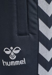 Black athletic shorts featuring white chevron patterns and a small white embroidered logo. Made from smooth, stretchy fabric.