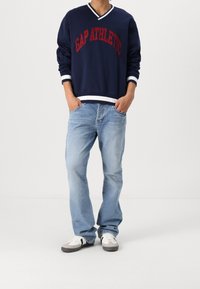 Granatowa bluza z kapturem z czerwonym napisem "GAP ATHLETIC", białe akcenty na kołnierzu i mankietach; jasnoniebieskie dżinsy; szare, białe i czarne tenisówki.