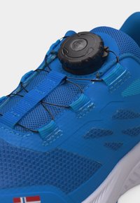 Zils sporta apavu ar sieta audumu, elastīgām šņorēm, kas pievilktas ar melnu diska bloķēšanas sistēmu, un nelielu Norvēģijas karogu uz zoles malas.