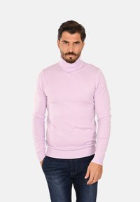 Maglione a collo alto di colore viola chiaro realizzato in materiale morbido con texture a costine. Design aderente, con maniche lunghe e orlo a costine. Indossato con jeans scuri.