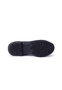 Suela de zapato de goma negra con patrón de relieve texturizado. Presenta un logo en la entresuela y surcos profundos para tracción.
