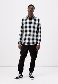 Zwart-wit geblokte flanellen shirt, lange mouwen, met knopenstijl, gecombineerd met zwarte tapershorts en zwarte sneakers. Eenvoudige stofstructuren.