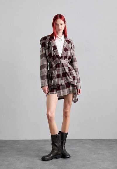 Blazer de cuadros con hombros con volantes, cintura ceñida y falda a juego. Presenta tonos grises, rojos y beiges; combinado con botas de cuero negras hasta la rodilla.