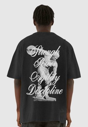Black oversized t-shirt featuring a textured print of a statue and the words "Strength, Power, Agility, Discipline" in white script.