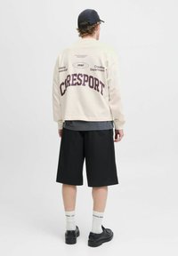 Creme sweatshirt med maroon "CRESPORT" tekst, sorte shorts og sorte sko. Plain sort kasket, hvide strømper med mærkets tekst. Fritidsoutfit.