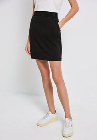 Jupe noire, longueur genoux, avec un waistband élastique et des poches latérales. Fabriquée en matériau doux, elle présente un design simple et épuré.