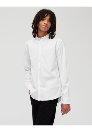 Chemise blanche à manches longues en coton avec col et coupe droite. Associée à un pantalon noir, offrant un design simple.