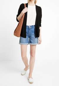 Black cardigan, white top, denim shorts with rolled hems, brown shoulder bag, and white espadrilles, displayed against a plain background.