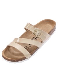 Beige patenterad konstläder sandal med två korsade remmar och en justerbar rem. Korkfotbädd och vit gummisula.