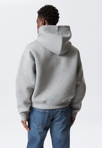 Grijze hoodie met een grote capuchon, geribbelde boorden en zoom. Gecombineerd met blauwe spijkerbroek, rugaanzicht tegen een effen achtergrond.