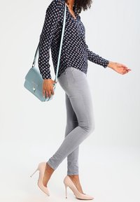 Blusa blu navy con motivo floreale, jeans skinny grigio chiaro, borsa a spalla azzurro chiaro e décolleté rosa pallido.