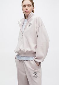 Lys rosa lynlås sweatshirt med høj krave, elastisk bund og et Paris-logo. Sammen med matchende bukser med sidelommer og logo detaljer.