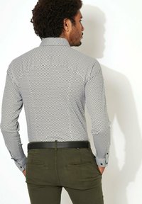 Heren overhemd met lange mouwen op een witte achtergrond, zwart cirkels patroon en met knoopmanchetten, gecombineerd met olijfgroene broek en een zwarte riem.