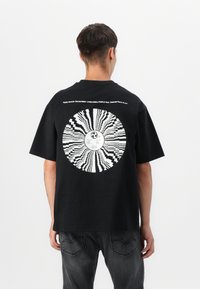 Black cotton t-shirt featuring a large white graphic resembling a vinyl record on the back, with text detailing a limited edition vinyl release.