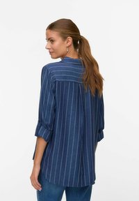 Marineblauwe shirt met witte verticale strepen, zachte stof, opgerolde mouwen, rimpel aan de achterkant en een kraag met knopen.