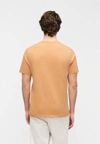 Μπλούζα με κοντά μανίκια σε ανοιχτό πορτοκαλί απόχρωση, με κλασική στρογγυλή λαιμόκοψη και λεία, απαλή υφή. Απλός σχεδιασμός χωρίς ορατά μοτίβα.